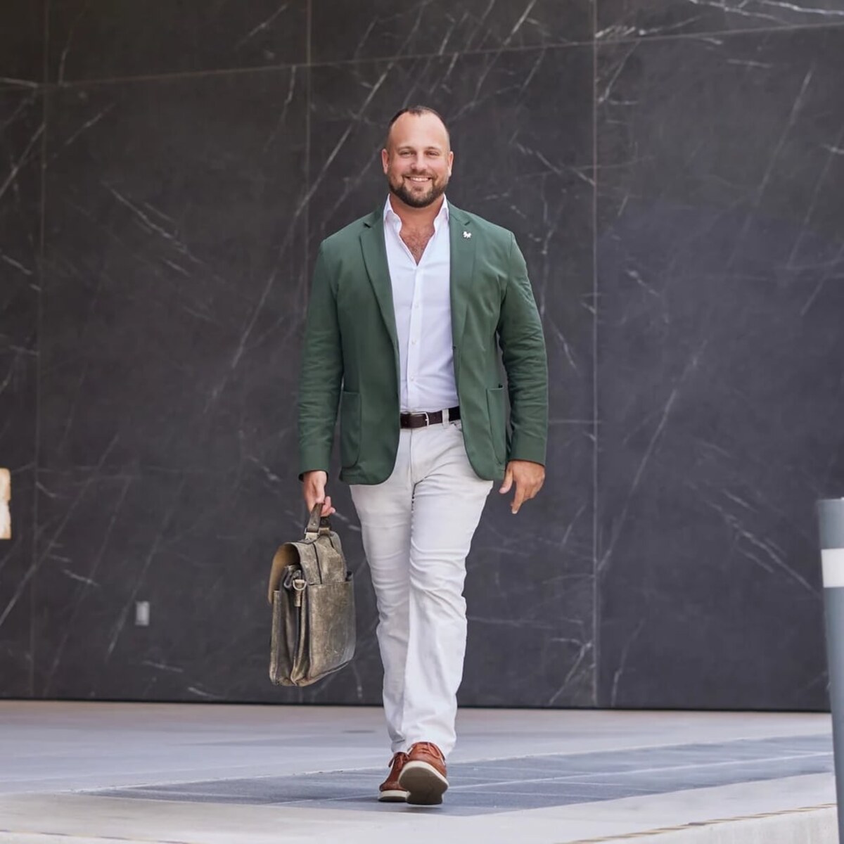 Adam Gurewicz walking past a marble facade in Fort Lauderdale, carrying a leather portfolio.
